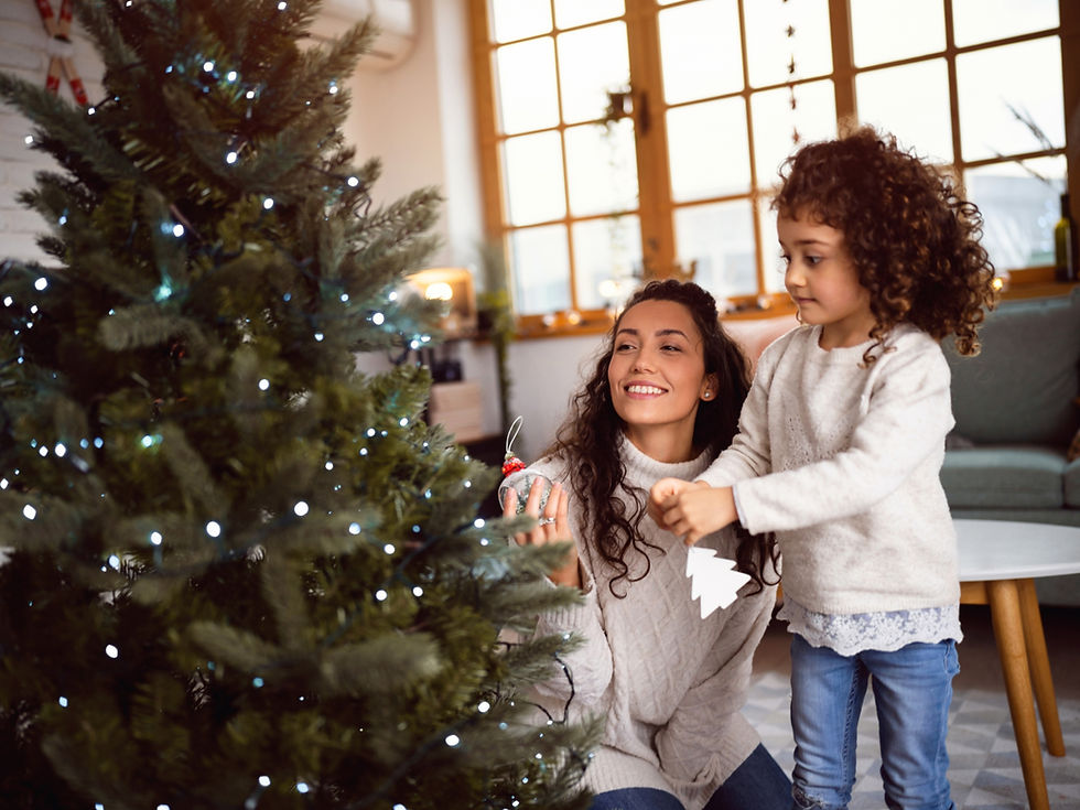 Photo of a woman and a girl hanging ornaments on a lit Christmas tree.