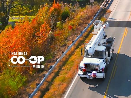 Overhead photo of an electric utility truck driving on a road with colorful fall trees in the background.