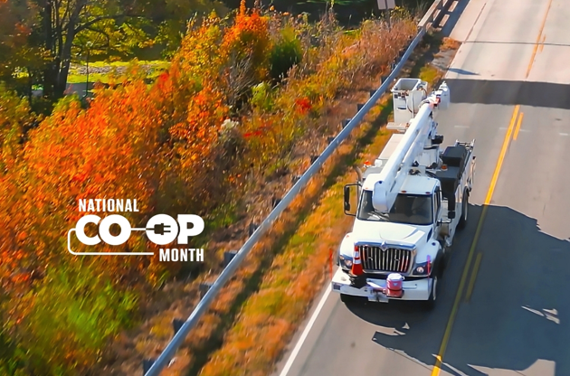Overhead photo of an electric utility truck driving on a road with colorful fall trees in the background.