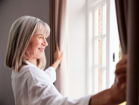 Photo of a smiling woman opening window curtains.