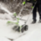 Photo of a person operating an electric snowblower on a snow-covered driveway.