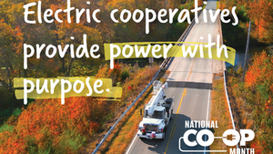 Overhead photo of an electric utility truck driving on a road with colorful fall trees in the background.