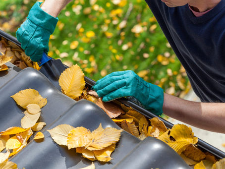 Photo of a person wearing gloves and cleaning out a gutter on a roof.