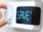 Close-up photo of a hand turning down a dial on a thermostat with the word “SAVE” on the thermostat digital screen.