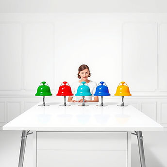 an all white desk in an all white room with different color bells on it, green, red, blue,