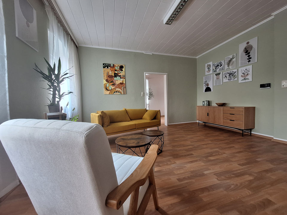 Ein modern und gemütlich eingerichteter Therapieraum mit einem weißen Sessel, einer gelben Couch und stilvoller Wanddekoration. Die beruhigende Atmosphäre spiegelt die einladende Umgebung der Heilpraxis Bayreuth für Psychotherapie (HPG) Bayreuth wider.