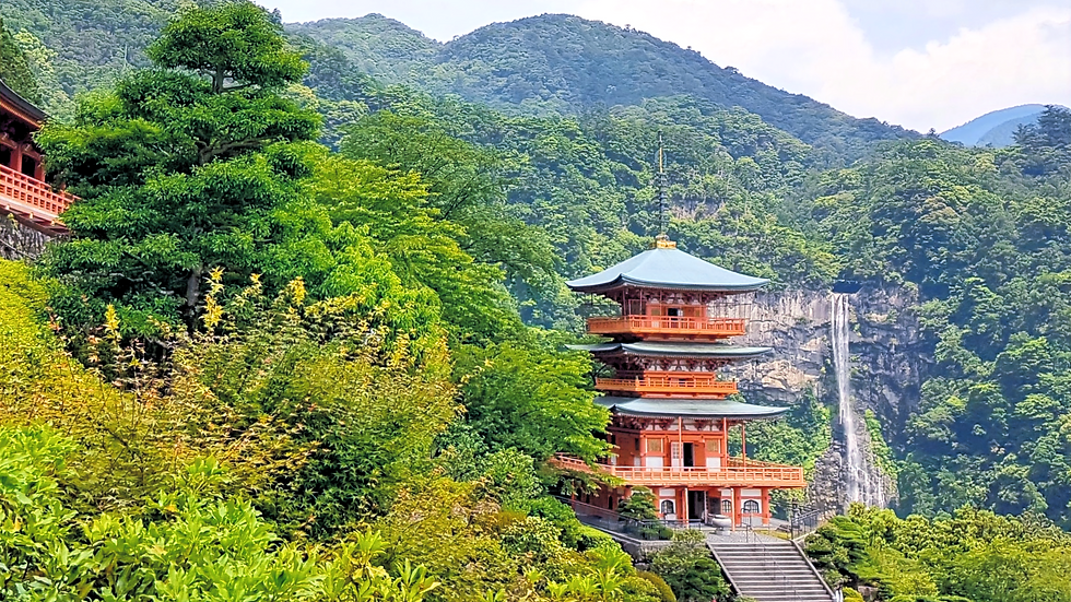 Montanhas cobertas de floresta, uma pagoda vermelha de 3 andares e uma cachoeira ao seu lado.