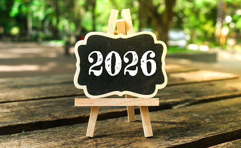 A small wooden chalkboard with the words “2026” written in white chalk, standing on a wood