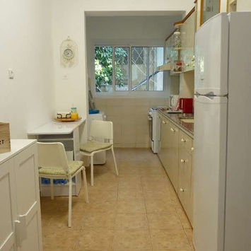 Узкая кухня с белым холодильником, светлыми шкафами и столом