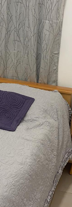 Спальня: кровать с серым покрывалом, тумбочка с лампой.