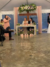 Bride and groom sitting at their table during the reception while someone gives a speech. Candles on the floor in front of them.