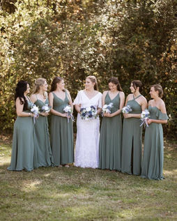 A bride stands in between her bridesmaids. The bridesmaids dresses are green and they all hold bouquets.