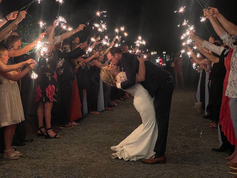 Groom dipping bride and kissing her in an aisle made by guests holding sparklers at night.