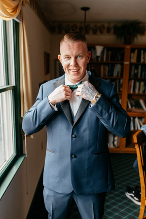 Groom in wedding suit adjusting his bowtie. 
