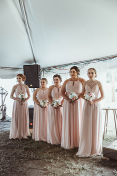 Wedding bridesmaids in dusty pink dresses standing in a line with floral bouquets