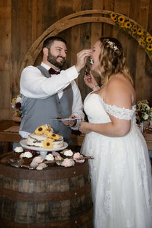 A bride and groom sharing the first slice of cake at the wedding reception. The groom is squishing the cake in the bride's face