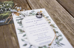 Wedding invitation on wooden table with wedding ring on top of it.
