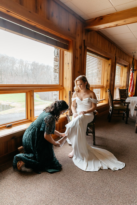 Bride in wedding gown getting help with putting her shoe on.