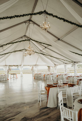 Wedding reception under white tent. Round tables with white chairs. 