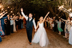 Bride and groom with hands in the air celebrating in front of guests outside.