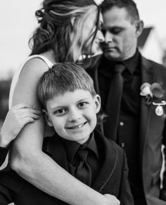 Black and white photo of bride and groom looking at each other while little boy in front of them smiles.