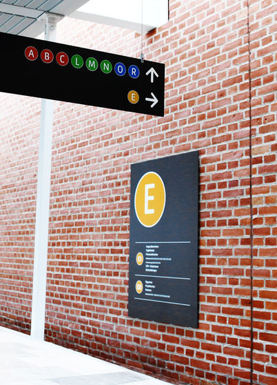 Nedhængsskilt med navigation og wayfinding til afdelinger på hospitalet samt et væghængt oversigtskort over afdeling E
