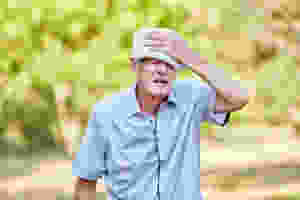 A senior man is trying to cool himself while walking outdoors in the summer heat.