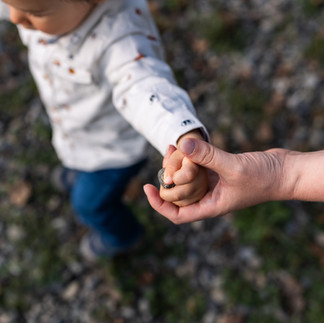 Mum holds toddlers hand during an outdoor walk. They ground is covered by round pebbles.