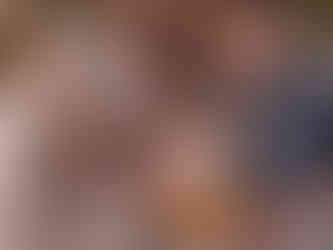 Family of five smiling, lying on grass. Baby in yellow, others in neutral tones. Warm, relaxed outdoor scene.