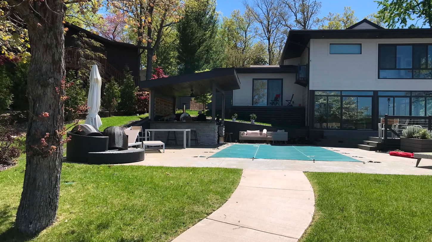 Custom outdoor living space with patio, covered kitchen area, and landscaped backyard at a modern lake home.
