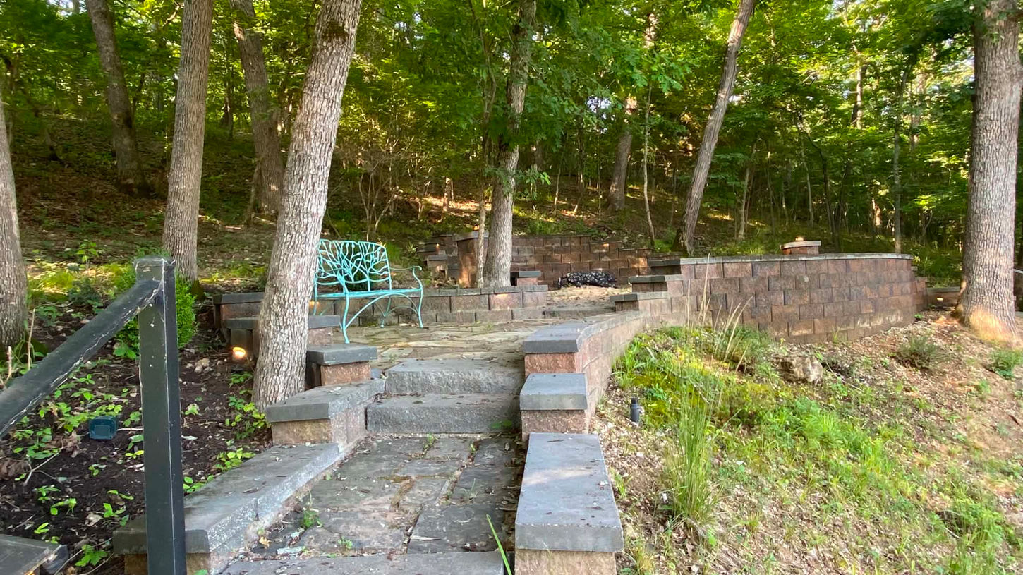 Outdoor entertaining area with custom hardscape design with curved retaining walls, stone steps in a natural area along the lakeside.