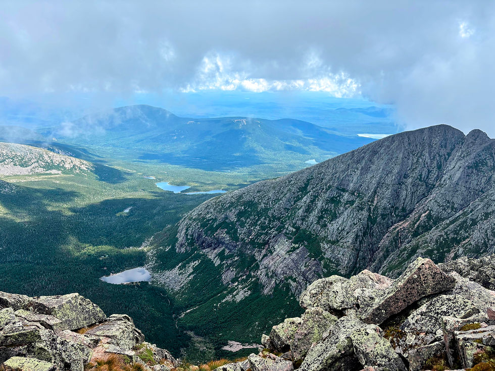 View from Baxter Peak: Chimney Pond and the basin rising up to Pamola Peak Mountains in the background with gray clouds hanging overhead.