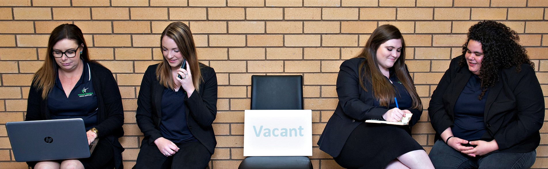 Hard at work staff sitting either side of a chair that holds a 'vacant' sign.