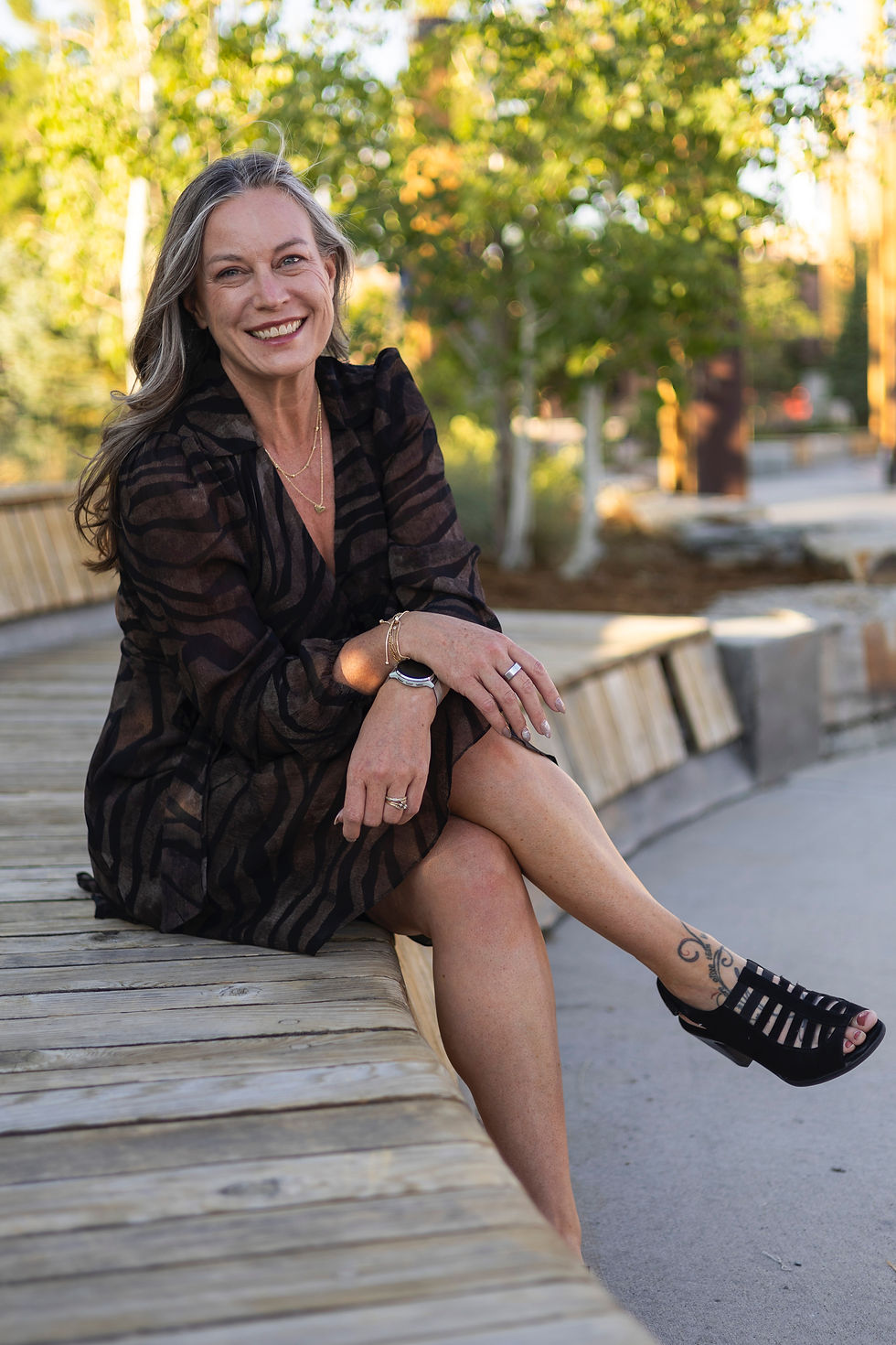 woman sitting outdoors with legs crossed, smiling at camera