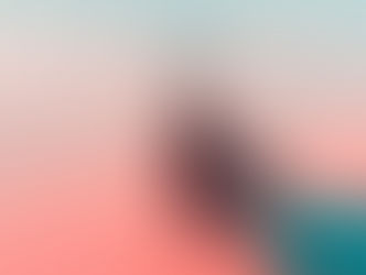 Hand holding a clear light bulb against a warm pastel gradient sky.