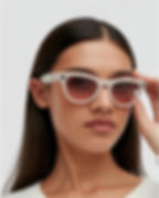 Person wearing white sunglasses with a neutral expression, adjusting the frames. White background. Brand logo visible on the glasses.