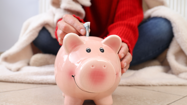 person wearing blanket putting money into piggy bank