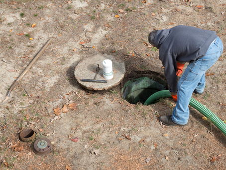 Worker using a large hose to pump waste from an open residential septic tank during a septic service appointment.