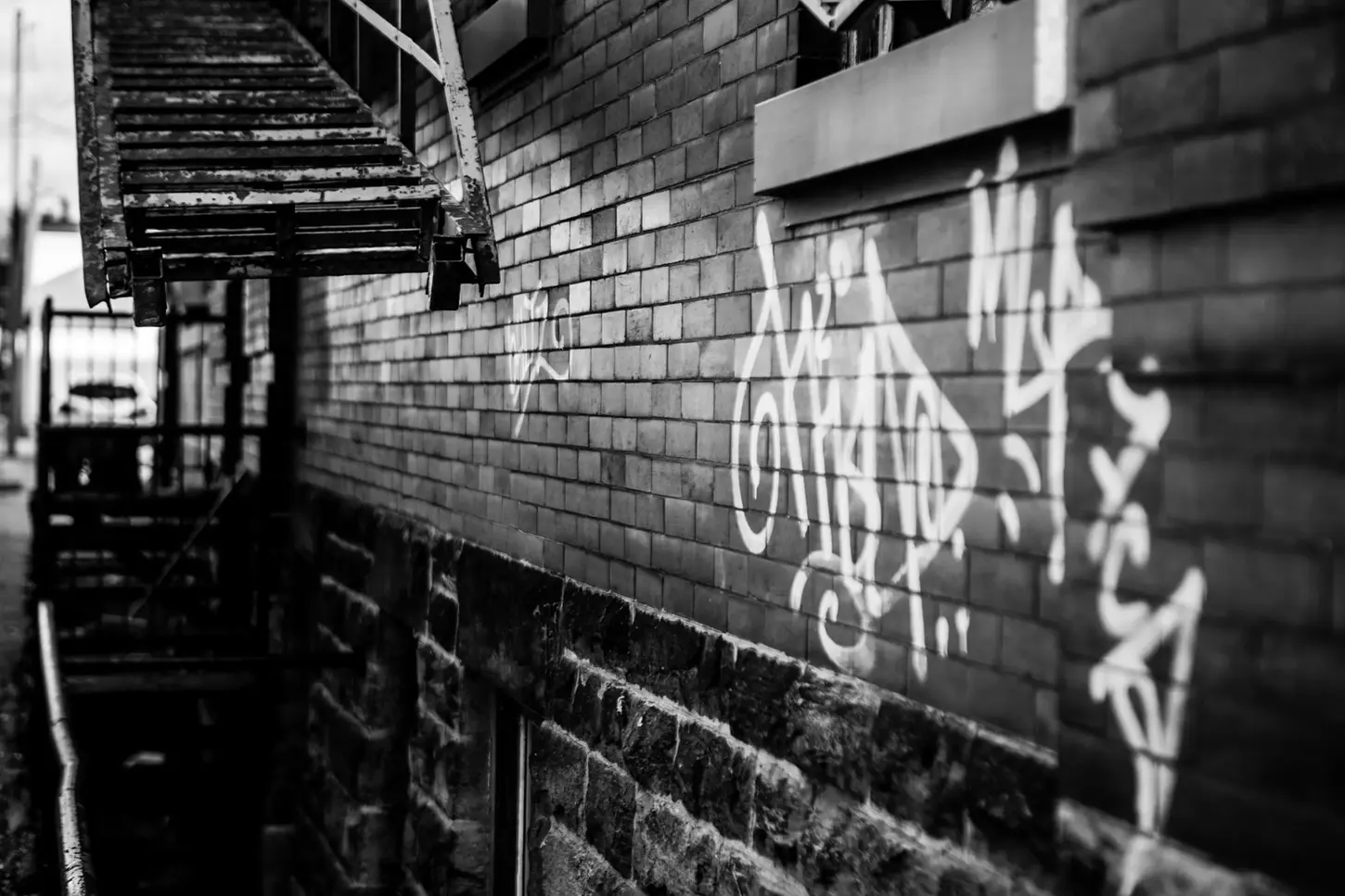Cityscape & Street Fine-Art Photography by Blake Ferguson demonstrate monochrome perspectives of a graffiti-marked alleyway with a fire escape in Downtown London, Ontario, Canada.