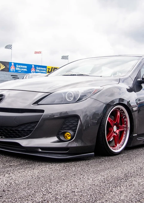 Modified dark gray Mazda 3 sedan, red wheels, Sprint banner background.