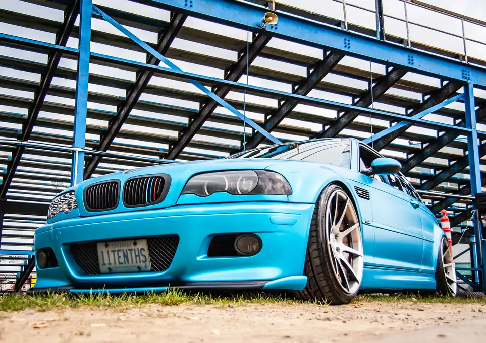 Blue BMW M3 car with 'OUTTNUS' license plate under bleachers
