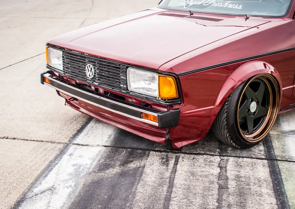 Lowered dark red Volkswagen car with custom bronze-lip wheels on pavement.