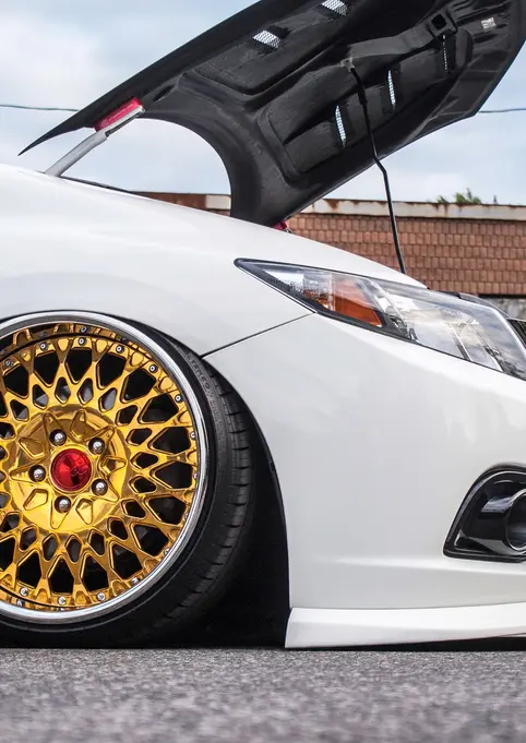 White lowered car, open hood, gold wheels at outdoor car show.