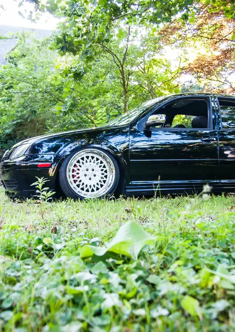 Black lowered Volkswagen Jetta with custom wheels parked on green grass.