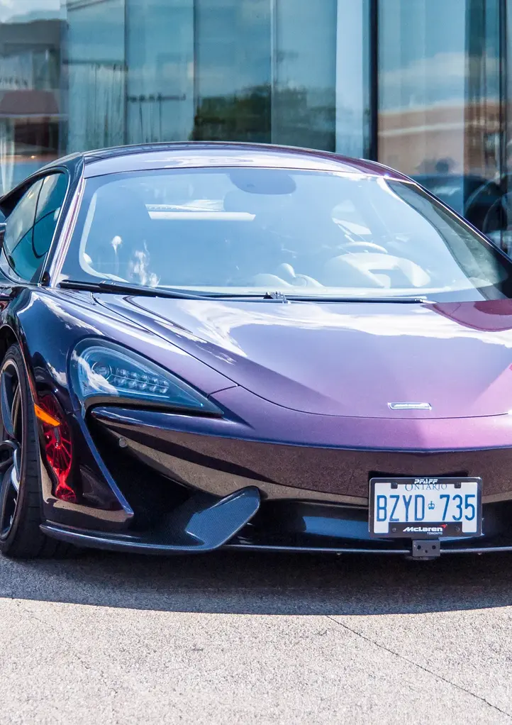 Purple McLaren sports car parked in front of a glass building outdoors.