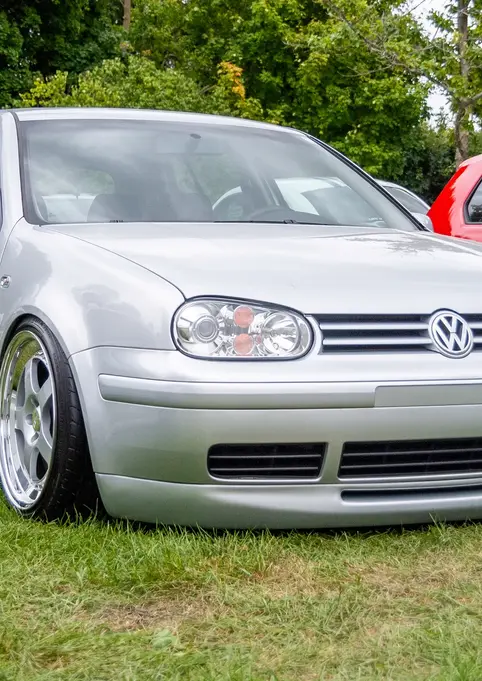 Silver Volkswagen Golf parked on grass, showcasing its customized wheels and body.