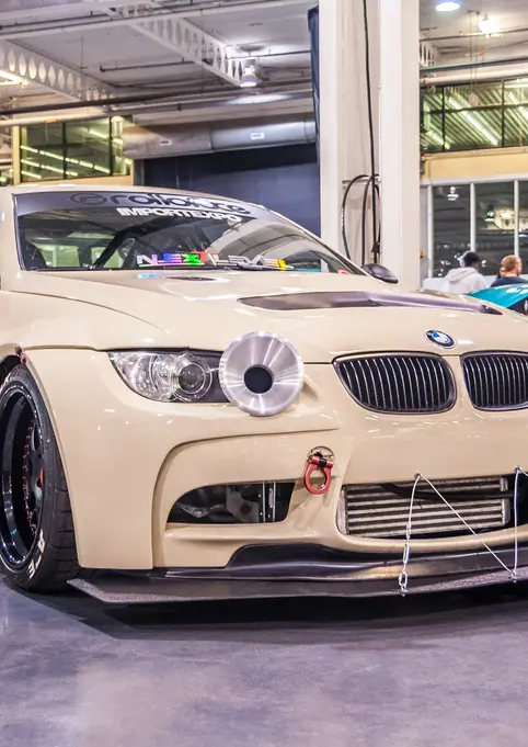 Custom cream BMW car with "SPEED HUNTERS" banner at indoor show.