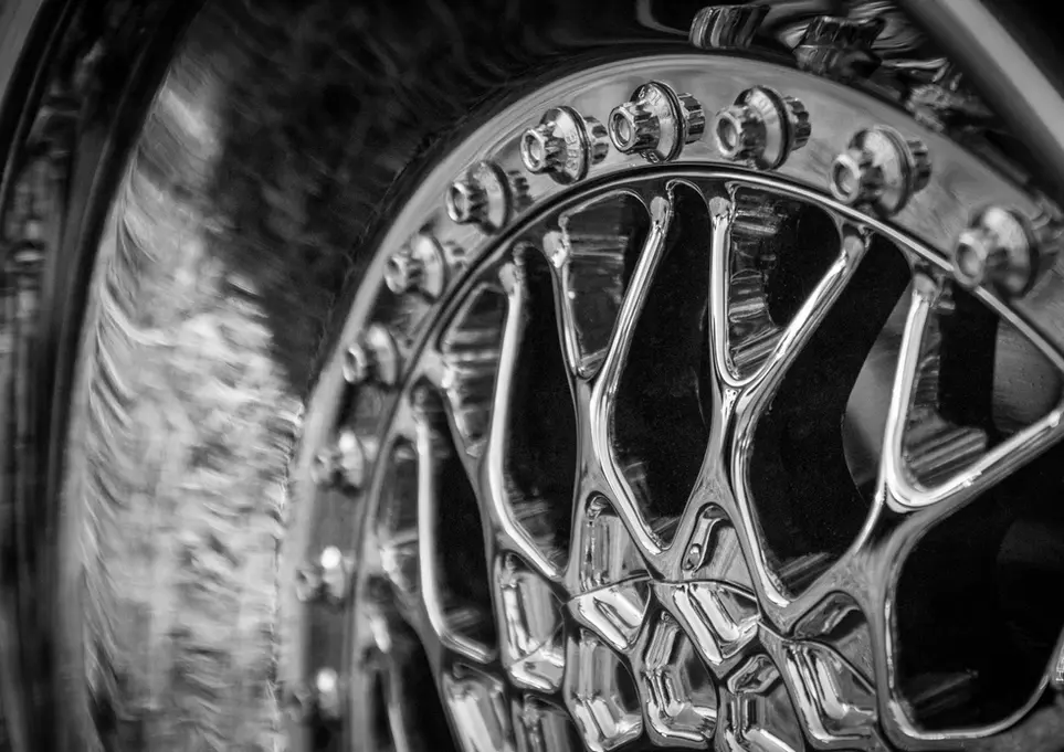 Black and white close-up of an intricate chrome car wheel.