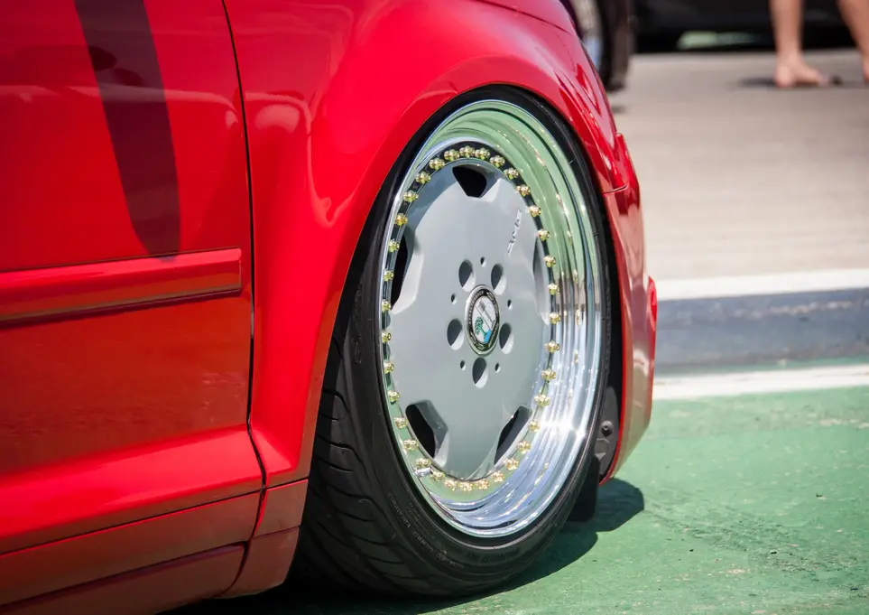 Red car's deeply stanced silver multi-spoke aftermarket wheel.