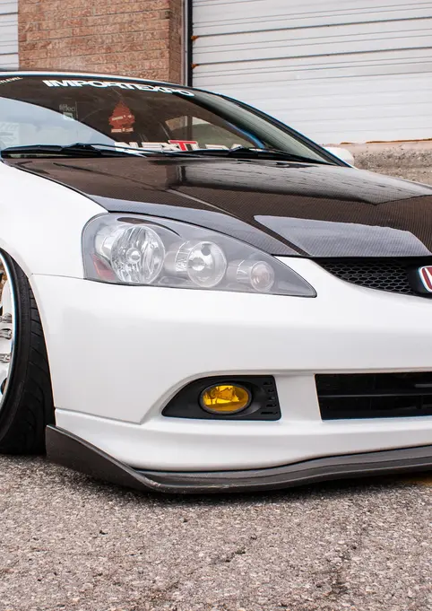 Stanced white Honda Integra RSX, black carbon hood, custom chrome wheels.